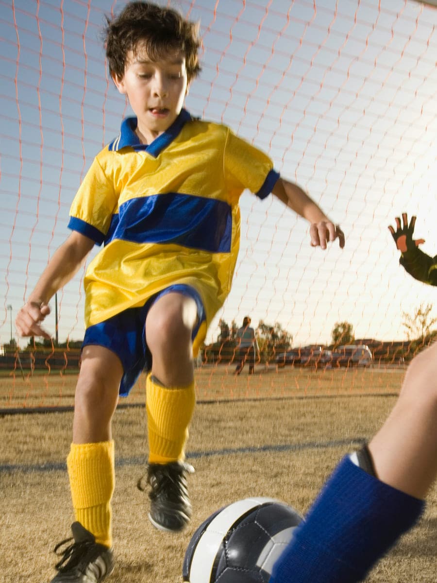 A boy in a yellow kit races towards the ball in front of the goal