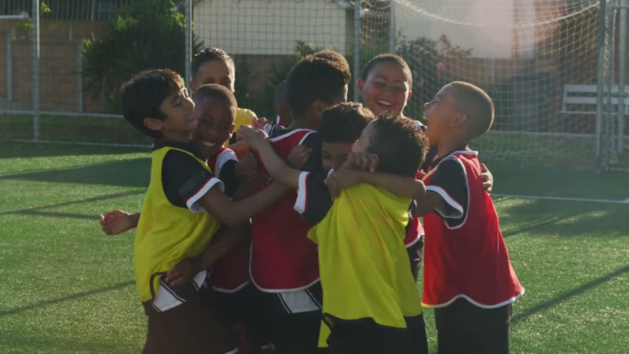 A youth team hugs and celebrates together on a sunny pitch